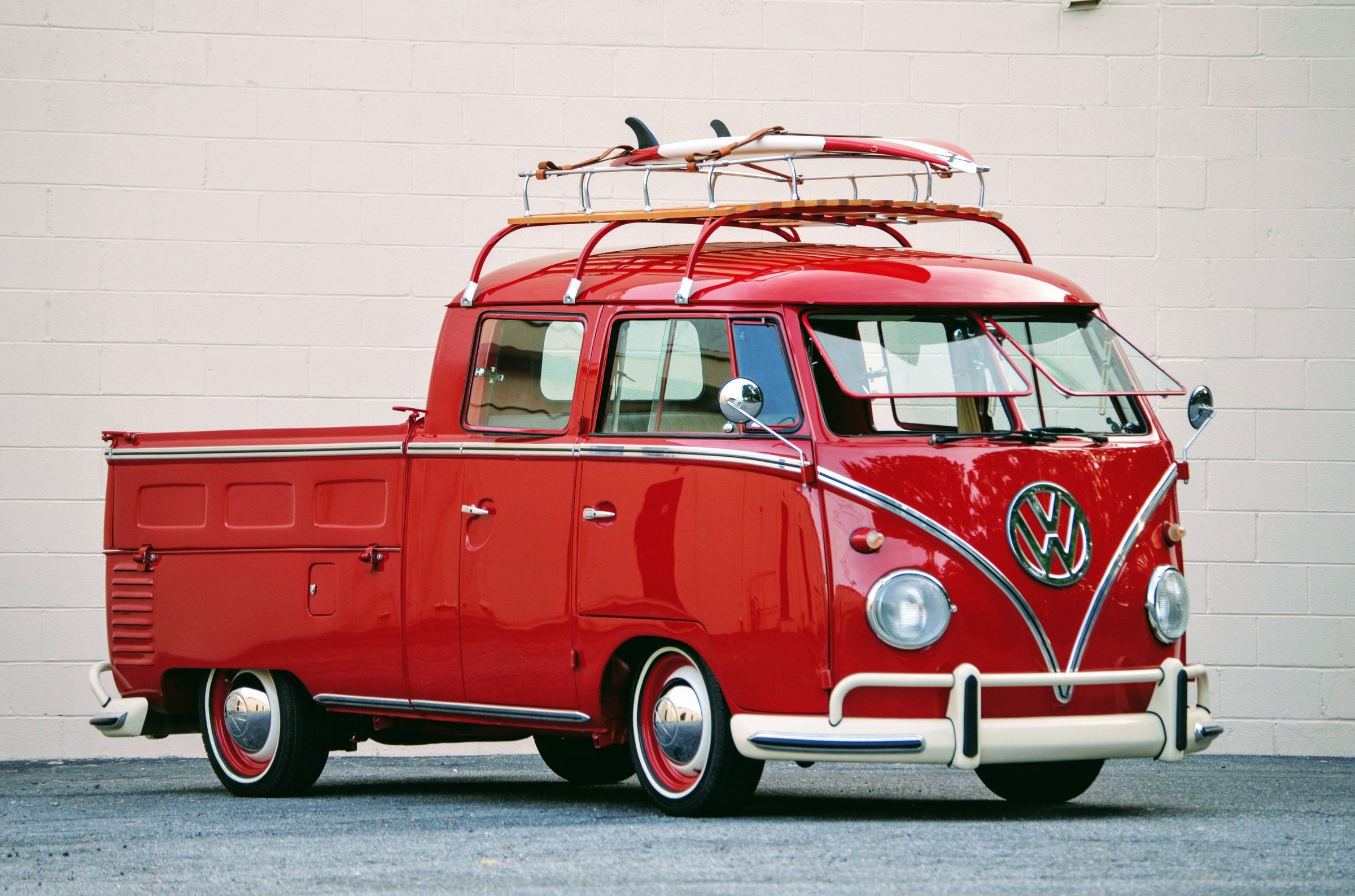 Red split-window Volkswagen Bus double cab pickup with roof rack and surfboard